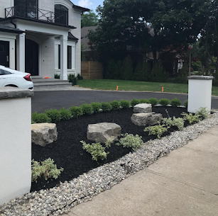 Fresh black mulch garden bed with boulders and shrubs along a driveway